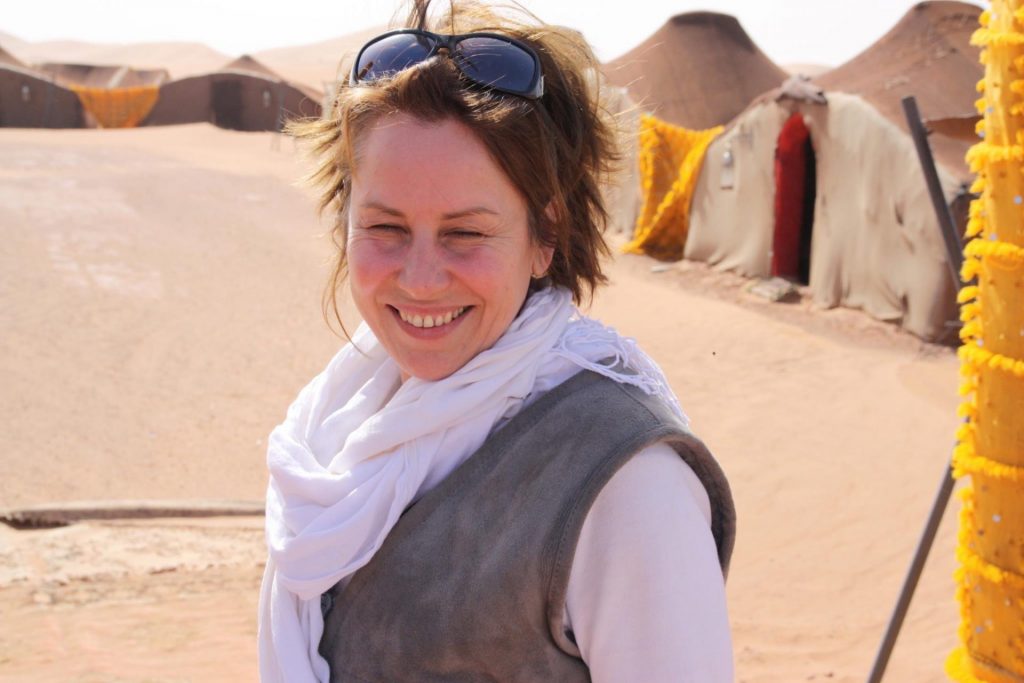 Im Wüstencamp in der Sahara steht eine glückliche Frau.